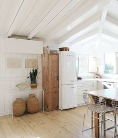 a kitchen with white walls and wooden floors has an island in the middle, while two stools sit on either side of the table