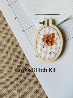 a cross stitch kit with an orange flower in the hoop on top of a piece of paper