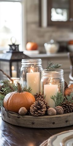 candles and pine cones are arranged in a tray on a dining room table with other decorations