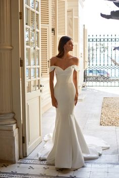 a woman in a wedding dress is standing by an open door and looking into the distance