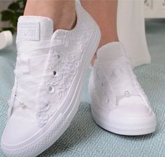 a woman's feet wearing white shoes with lace and pearls on the side, sitting on a bed