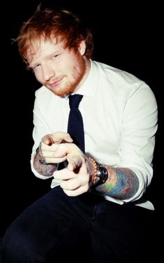 a man with red hair wearing a white shirt and black tie holding his wrist tattoo