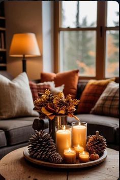 candles and pine cones sit on a tray in front of a couch