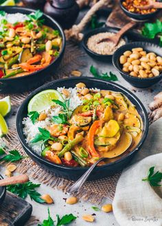 thai food is served in black bowls and garnished with cilantro, pine nuts, cashews, and lime