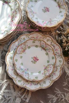 four plates with flowers on them sitting on a lace tablecloth next to pine cones