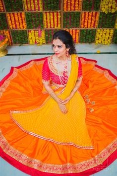 a woman in an orange and yellow sari sitting on a round rug with flowers behind her