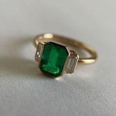 an emerald and diamond ring on a white surface