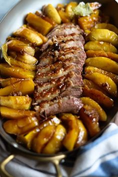 a pan filled with meat and potatoes on top of a blue table cloth next to a fork