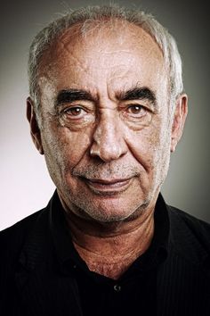 an older man with gray hair and black shirt looking at the camera while wearing a collared shirt