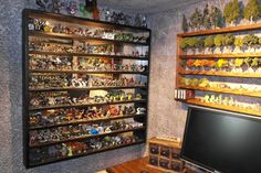 a desk with a monitor and shelves full of toy figurines on the wall