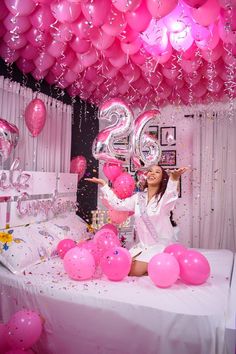 a woman sitting on top of a bed surrounded by pink balloons