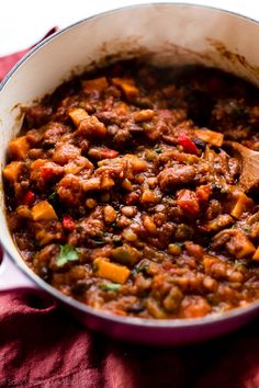 a pot filled with meat and vegetables on top of a red cloth next to a wooden spoon