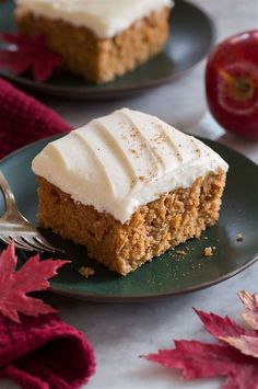 two pieces of cake on black plates with white frosting and an apple in the background