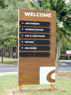 a welcome sign in front of a park with trees and bushes behind it that reads, link parking worship center amc & lighthouse office offices deliverries