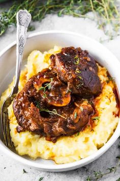 a white bowl filled with mashed potatoes topped with meat and garnished with herbs