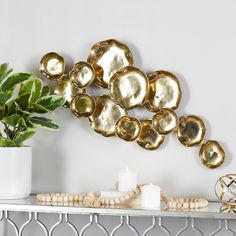 a white shelf topped with lots of gold plates next to a potted green plant