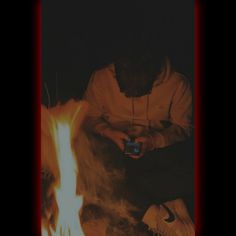 a man sitting in front of a fire holding a cell phone