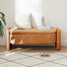 an orange couch sitting on top of a white rug next to a plant and shoes