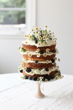 a cake with white frosting and blueberries on top is sitting on a table in front of a window