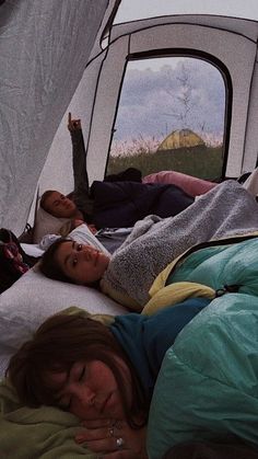 two women laying on a bed in front of a tent with the door open and one woman sleeping next to her