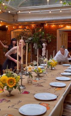 two women and one man are setting the table for a meal with sunflowers