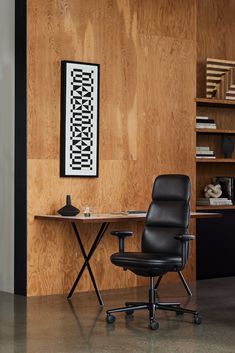 an office chair sitting in front of a desk with a book shelf and art on the wall