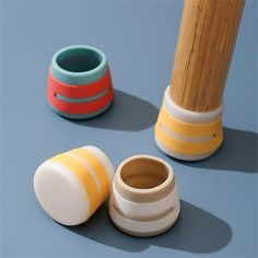 three different colored vases sitting next to each other on a blue surface with a wooden pole in the background