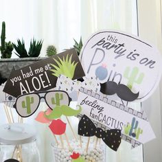 a table topped with lots of cupcakes and cake toppers next to a potted plant