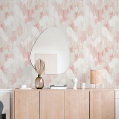 a dresser with a mirror and vase on it in front of a wallpapered background