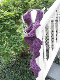 a purple crocheted scarf hanging from the side of a white porch railing next to shrubbery