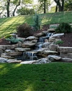 there is a small waterfall in the middle of this garden with rocks and grass around it