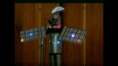 a toy windmill with lights on it in the shape of a robot standing next to a wooden door