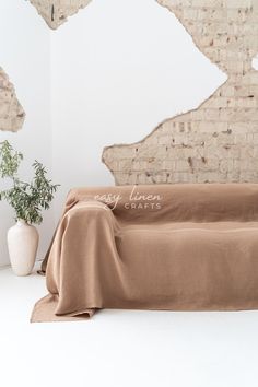 a couch covered with a blanket in front of a brick wall and potted plant