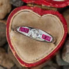 a diamond and ruby ring sits in a heart shaped box with stones on the ground