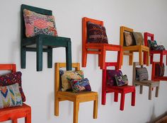 several colorful chairs are lined up against a white wall with pillows on the back and sides