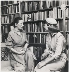 two women sitting in front of a bookshelf talking