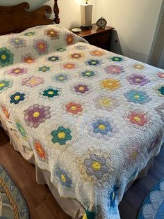 a bed with a flower quilt on it and a night stand next to the bed