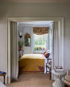 a bed sitting under a window in a bedroom next to a chair and table with a lamp on it