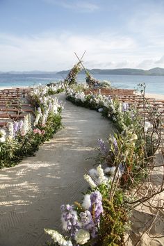 an outdoor ceremony set up on the beach with flowers and greenery in front of it