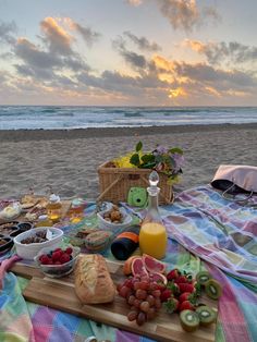 a picnic is set up on the beach with fruit, bread and juice in front of the ocean