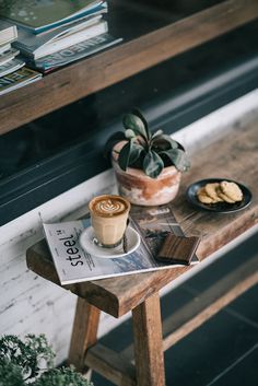 a wooden table topped with a cup of coffee next to a plate of cookies and a potted plant