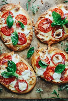 four small pizzas with cheese, tomatoes and spinach leaves on a baking sheet