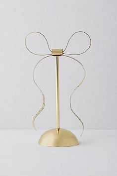 a gold candle holder with a bow on it's top and a white wall in the background