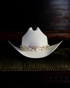 Capri Staple features two layers of gold hoop chain affixed with fresh water pearls on a white canvas cowboy hat. Proudly American Made. Our hats are manufactured in Mexico and details added by hand in Los Angeles, CA using the highest quality materials. Sizing S/M 19in-22.75in | 48cm-57.5cm L/XL 19.5in-23.25in | 49.5cm-59cm *Please allow up to 2 weeks for production and shipping. Luxury White Fedora For Western-themed Events, Cowboy Hat Display Ideas, Luxury White Adjustable Hat, Gold Western Hat Band For Kentucky Derby, Western Gold Hat Bands For Kentucky Derby, Luxury High Crown Adjustable Hat Bands, Luxury Adjustable Hat For Country Events, Elegant White Hat Bands For Rodeo, Elegant White Hat Band For Rodeo