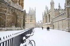 a bike parked on the side of a snow covered road next to a fence and buildings