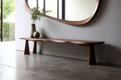 a wooden bench sitting under a round mirror next to a vase with a plant on it