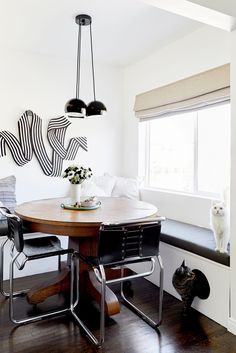 a dining room table with two chairs and a cat sitting on the floor next to it