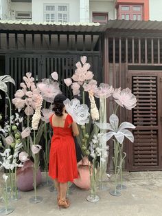 a woman in a red dress standing next to vases with flowers