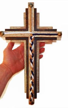 a hand holding a wooden cross that is made out of rope and wood planks