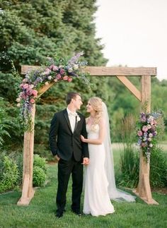 a bride and groom are standing under an arch with flowers on it in the grass